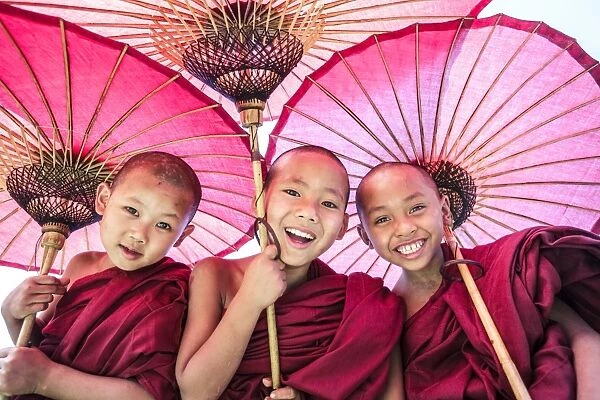 Myanmar, Mandalay division, Bagan. Portrait of three novice monks under red umbrellas