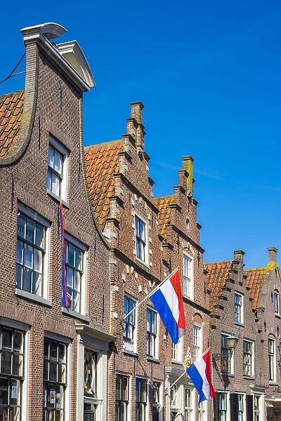Netherlands, North Holland, Edam. Brick houses with Dutch flags hanging outside for