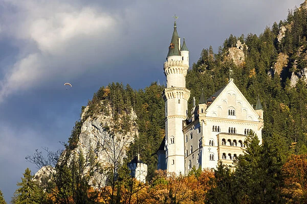 Neuschwanstein Castle framed by paraglide in the cloudy sky and the colorful woods