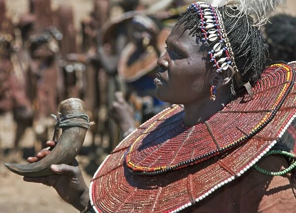 During a Ngetunogh ceremony, the mother of a Pokot initiate sings and dances holding the cowhorn container she used to smear fat over the masks of her son and other boys as