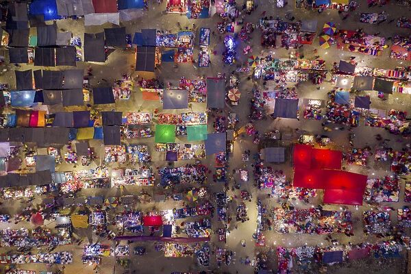 Night aerial view of people trading at weekly market, seeking out products in the city of