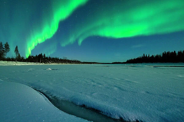 Northern Lights glowing bright over the snowy forest and frozen river in winter, Levi, Kittila, Lapland, Finland