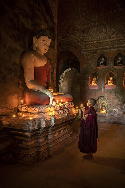 A novice monk holding a burning candle while praying by Buddha statue, UNESCO, Bagan