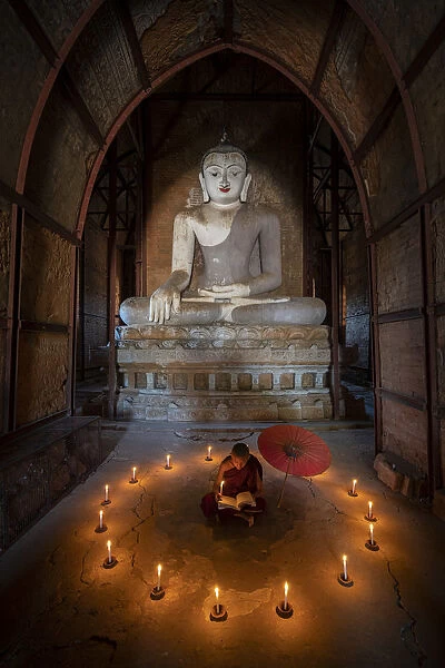 Novice monk studying inside a temple under big Buddha statue, UNESCO, Bagan