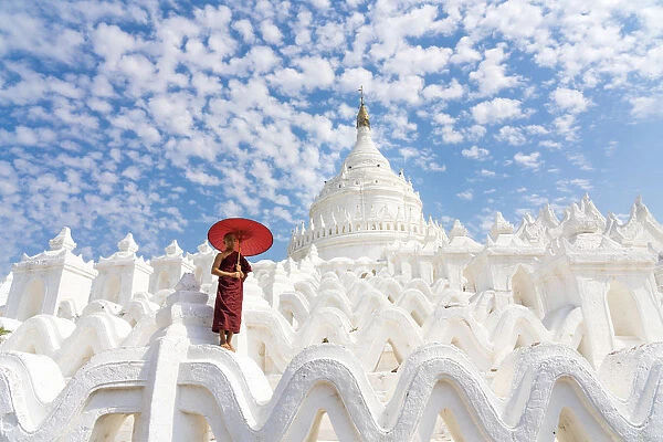 Novice monk with an umbrella standing at white Hsinbyume pagoda