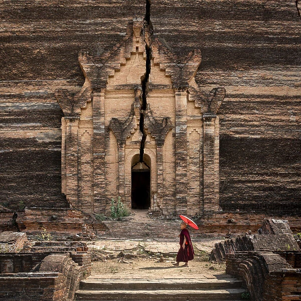 Novice monk walking towards unfinished Pahtodawgyi pagoda known for a crack caused by a