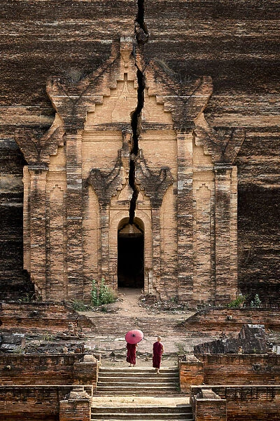 Two novice monks walking towards unfinished Pahtodawgyi pagoda known for a crack caused