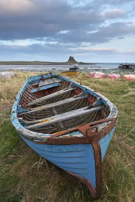 Framed Print : Old fishing boat pulled up on the shore at Holy Island, with the castle across the bay