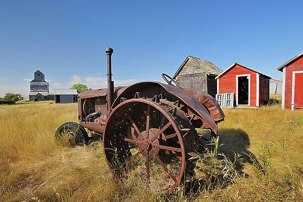 Old tractor, sheds and grain elevator in ghost town Fusiller Saskatchewan, Canada