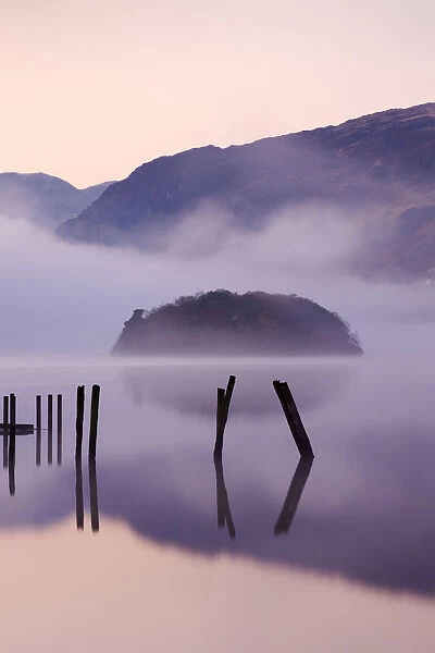 Old wooden jetty and St Herberts Island on Derwent Water at dawn on a misty