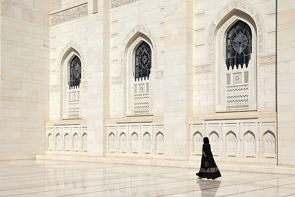An Omani woman walks past the marble facade of Sultan Qaboos Grand Mosque, Muscat, Oman