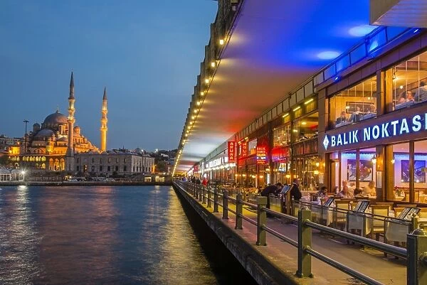 Outdoor restaurants under Galata Bridge with Yeni Cami or New Mosque in the background at dusk