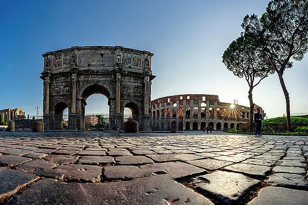 Panoramic of Coliseum and Arch of Constantine lit by sun rays at dawn, Rome, Italy