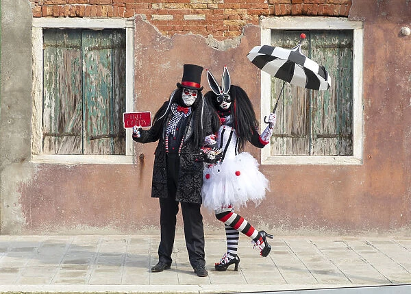 Two people pose in front of a colourful facade on Burano during the Venice Carnival