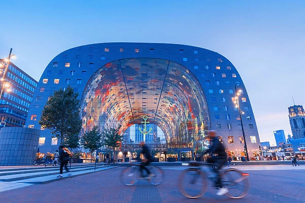 People riding bikes in front of the Market Hall in Rotterdam on a summer evening