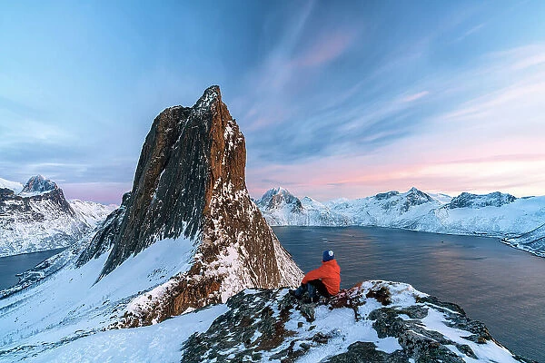 One person contemplating the sky at sunset sitting on a snowy ridge on Segla mountain, Senja, Troms county, Norway