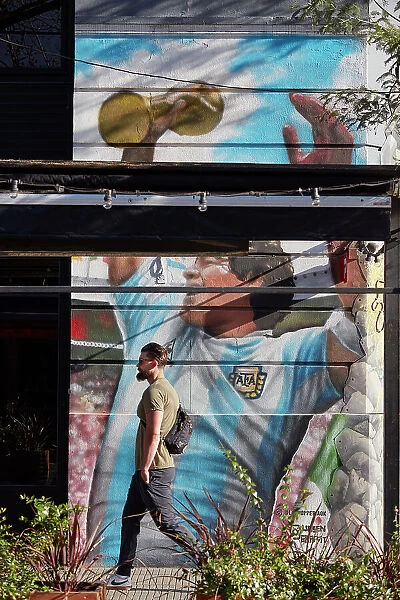A person passing by a wall art mural of Diego Armando Maradona in the district of Palermo, Buenos Aires, Argentina