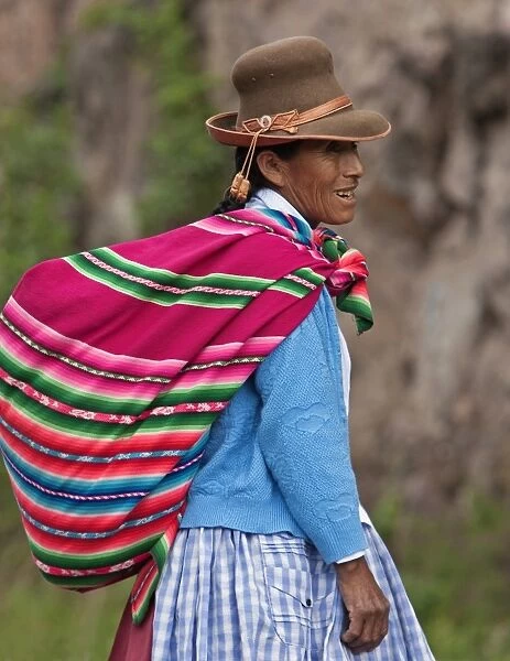 Peru. An Indian woman wearing a felt hat carries her farm produce to market in a brightly coloured blanket