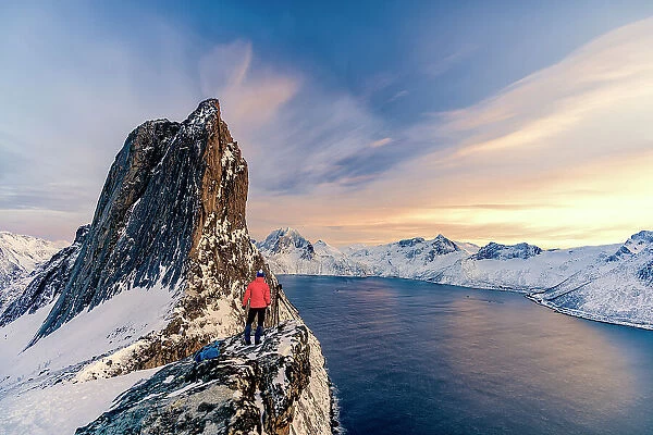 Photographer admiring Segla mountain peak covered with snow standing on top of rocks at sunset, Senja, Troms county, Norway