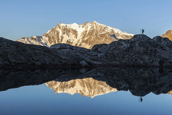 Photographer on rocks admiring Monte Rosa mirrored in water from Monte Moro Pass