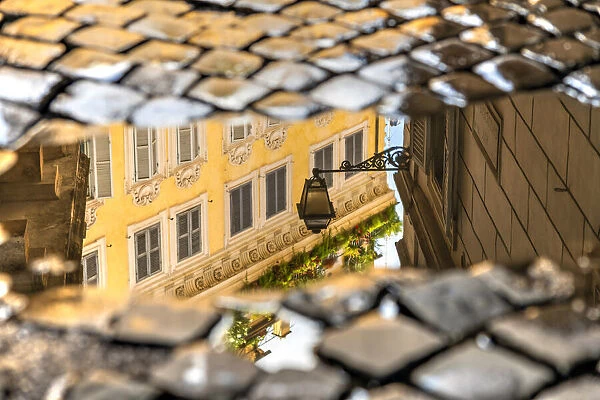 Picturesque corner of the old town reflected in a puddle on a cobbled street, Rome, Lazio