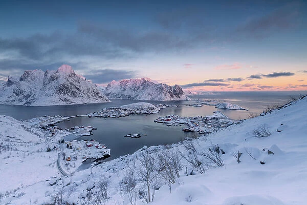 The pink colors of sunset and snowy peaks surround the fishing villages Reine Nordland