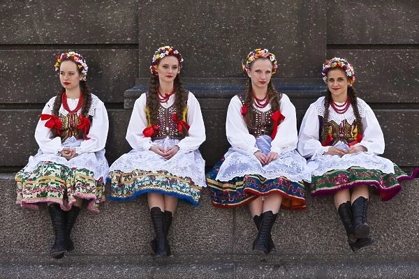 Poland, Cracow. Polish girls in traditional dress sitting at the base of the statue of Adam Mickiewicz, preparing to dance in