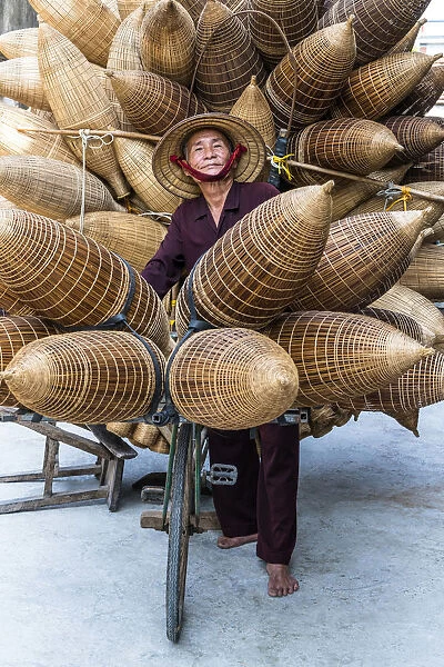 A portrait of a man on the bicycle loaded with the conical bamboo fish traps, near Hanoi