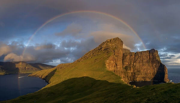 A full rainbow at sunset over the cliffs in Vagar. Faroe Islands