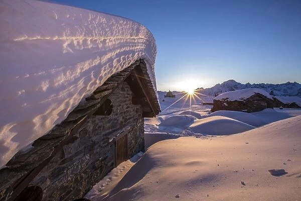 The last rays of sun light up the Prabello alp chalets covered with snow