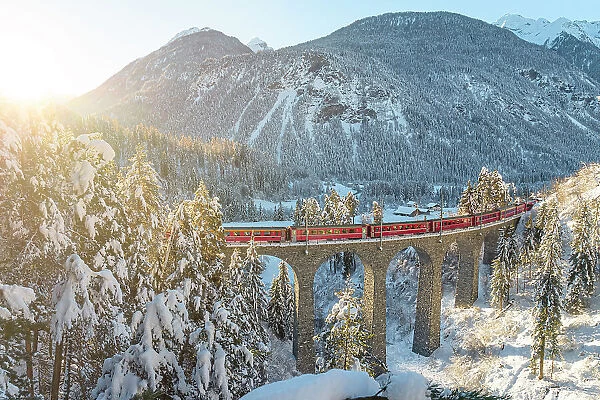 Red train traveling in the winter snowy landscape from Filisur to Tiefencastel railway station, aerial view, Graubunden, Switzerland