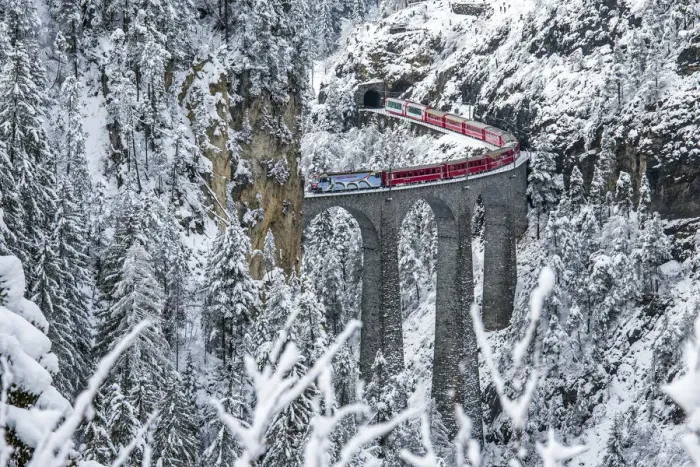 Framed Print : Red train Travelling on the Landawasser Viadukt through the vegetation covered in snow