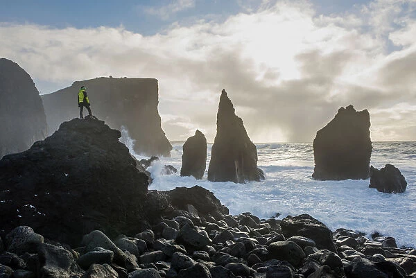 Reykjanes peninsula, Iceland, Europe. Man on top of a rock watches the waves of the ocean