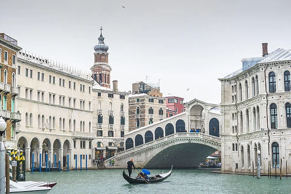 Rialto bridge, Venice, Veneto, Italy. Tourists on gondola under a snowfall