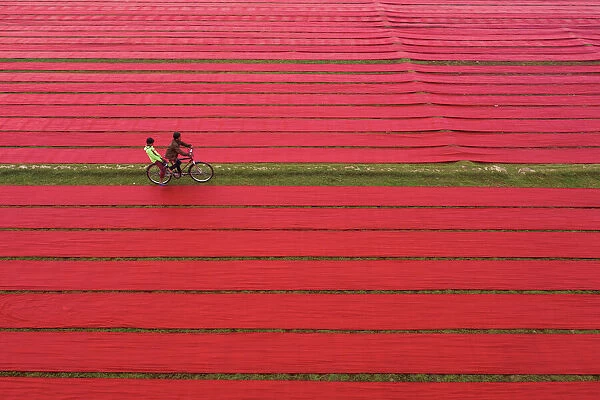 Riding bicycle middle of the drying red fabrics under sunlight, Narsingdi, Bangladesh