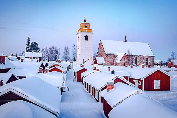 Roofs of cottages and bell tower covered with snow in the picturesque village of Gammelstad Church Town at dusk, Lulea, Sweden
