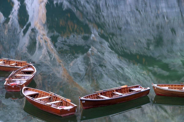 Row boats floating in the Braies lake on a calm morning, with the mountains reflecting in the water. Dolomites, Italy