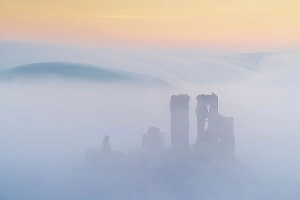 The ruins of Corfe Castle emerging from mist at dawn, Corfe Castle, Dorset, England. Winter (February) 2023