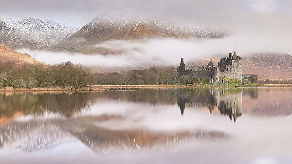 The ruins of Kilchurn Castle reflected in Loch Awe at dawn on a misty morning in the Scottish Highlands, Argyll and Bute, Scotland. Winter (March) 2017