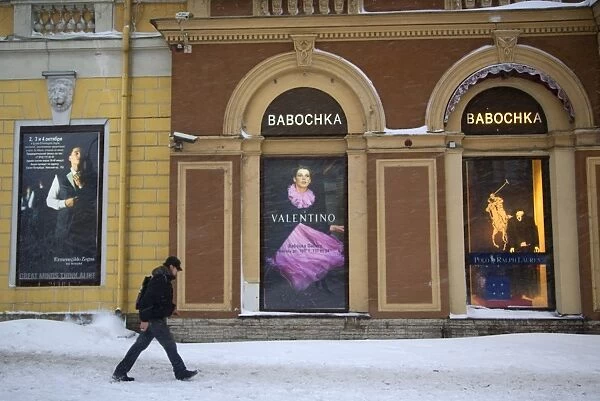Russia, St. Petersburg; A man walking in front of high end clothes adverts in the city centre in Winter