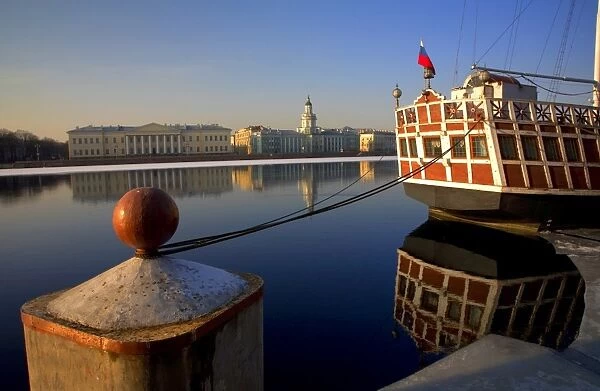 Russia, St. Petersburg; A wooden ship at pier on the partly frozen Neva River with the Kunstkamera in