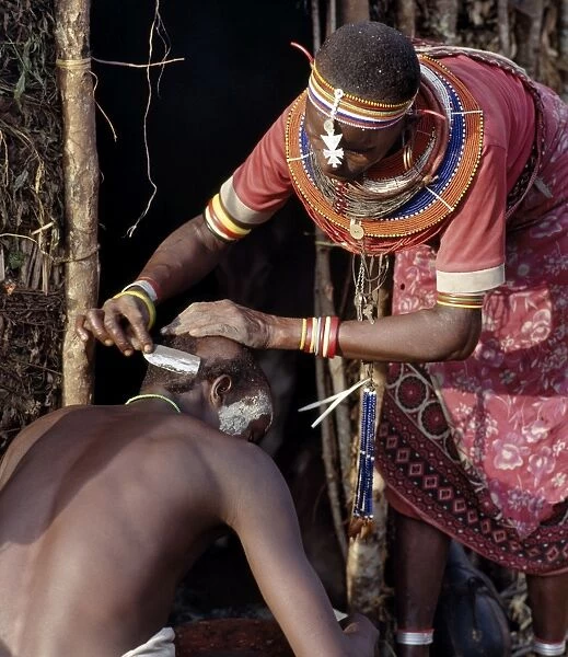 A Samburu mother shaves her sons head outside