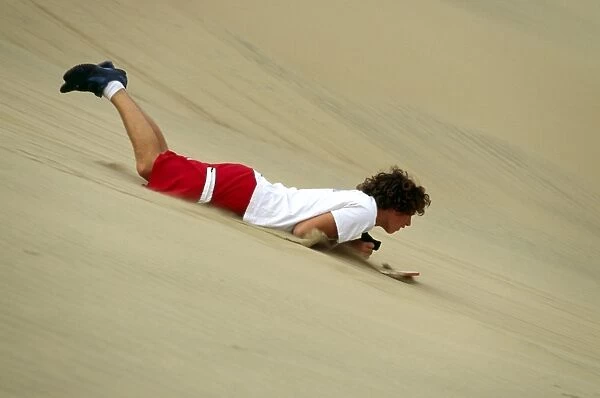 A sandboarder speeds down a dune head first