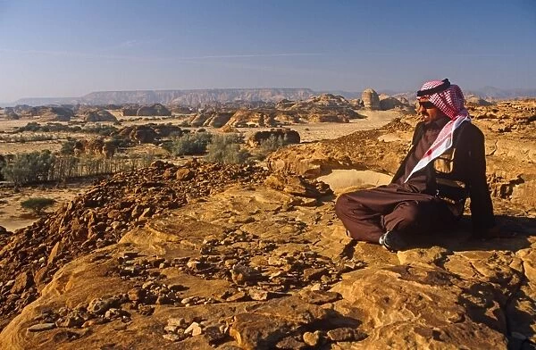 Saudi Arabia, Madinah, nr. Al-Ula, Madain Saleh (aka Hegra). A Saudi man gazes at stark cliffs