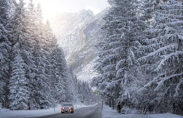 Scenic route with red car and snowy winter landscape, Dolomites Alps, Italy