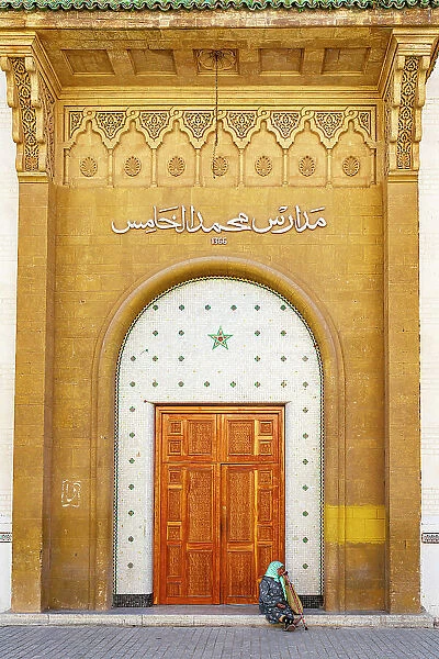 Senior woman with hijab sitting outside a doorway at majestic gold colored entrance of medina, Rabat, Morocco