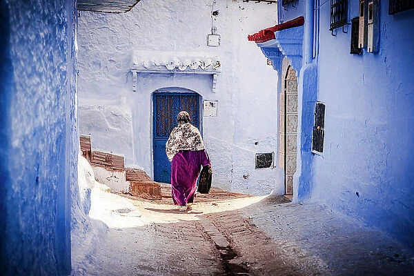 Senior woman with hijab walking among blue buildings of medina, Chefchaouen, Morocco