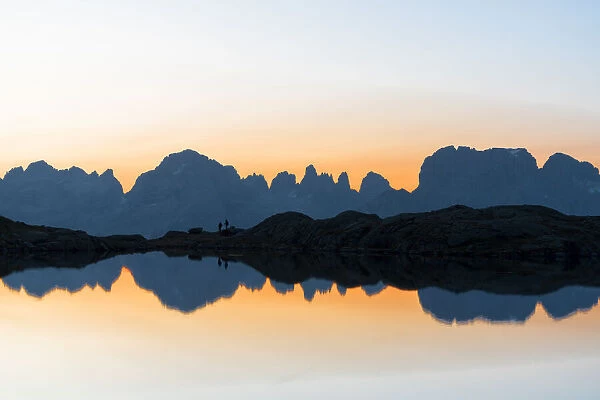 Silhouettes of hikers admiring Brenta Dolomites at dawn from Lago Nero di Cornisello