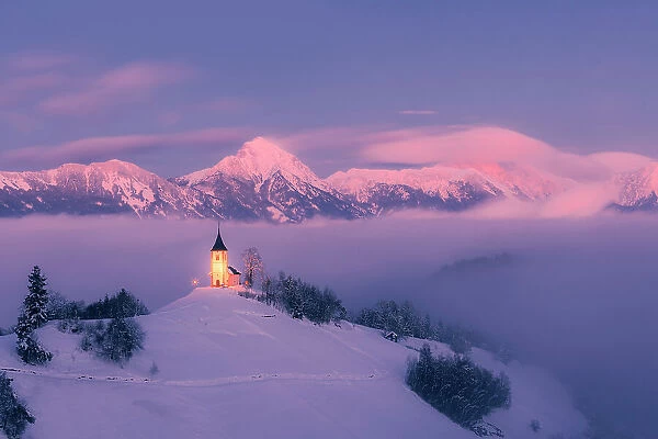 Slovenia, Jamnik, Church of St. Primoz covered with fog at dusk with the Kamnik-Savinja Alps beyond, Gorenjska
