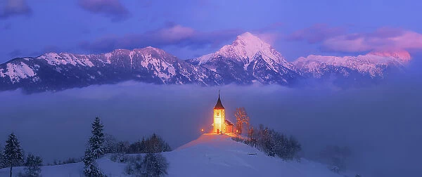 Slovenia, Jamnik, Church of St. Primoz covered with fog at dusk with the Kamnik-Savinja Alps beyond, Gorenjska